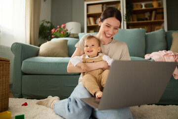 Cute baby boy and his mother sitting on the floor in the living room and using laptop