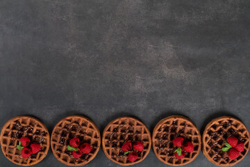 Desert Cacao round waffles with raspberries. Dark gray background. Top view. Copy space
