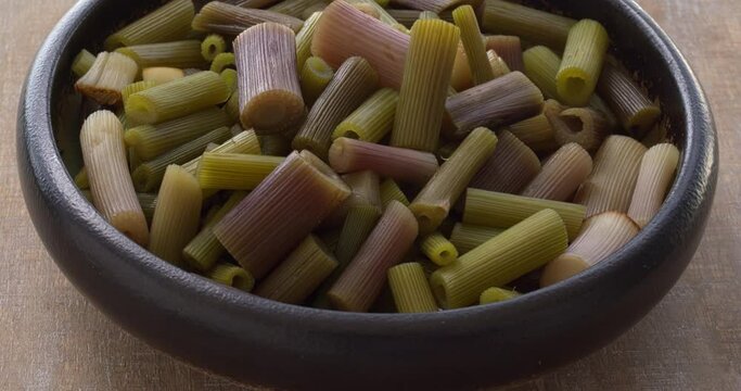 Boiled lovage herb young stalks in a bowl. Cooked fresh organic green vegetables. Table spin.