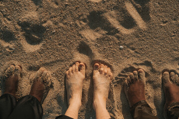 Three pairs of bare feet black and white skin different race nationality friends on sea shore sand