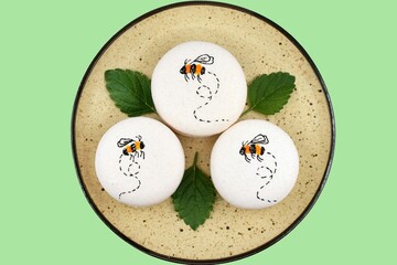 Macarons with flying bee, and lemon balm leaves on a plate, isolated on green background