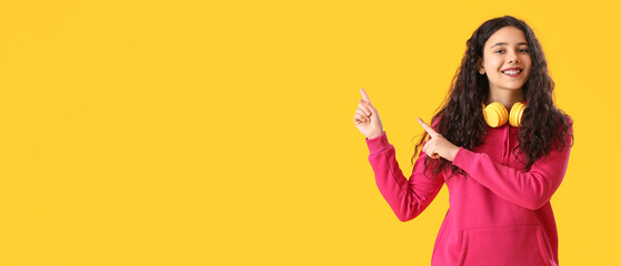 Teenage girl with headphones pointing at something on yellow background with space for text