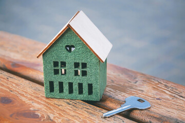A small house model and a key on wooden background, selective focus.	