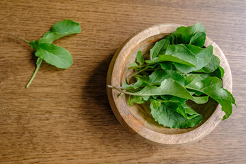 close up of arugula in a bowl with a walnut wood background