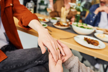 cropped view of gay man holding hand on boyfriend in wedding ring near blurred supper and parents...