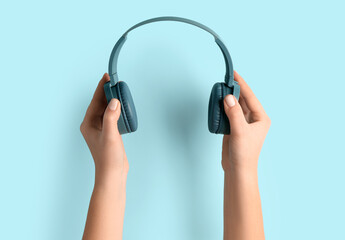 Woman holding modern headphones on blue background