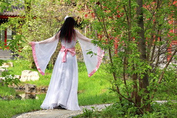 Obraz na płótnie Canvas Girl in a traditional asian dress standing in garden on pagoda background, rear view. Cherry blossom season, asian beauty and culture
