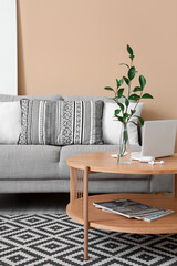 Coffee table with modern laptop, earphones and vase in interior of living room