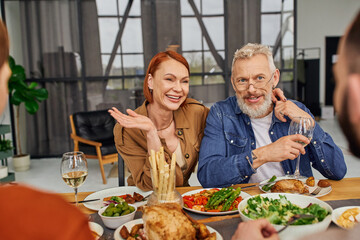 pleased parents smiling near blurred gay couple during family supper in living room. 