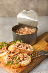 Board with delicious tuna bruschettas and tin can on grey table