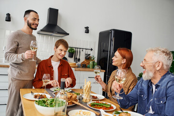 happy man toasting with wine during supper with gay partner and parents at home. 