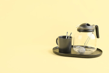 Tray with teapot and mug on yellow background