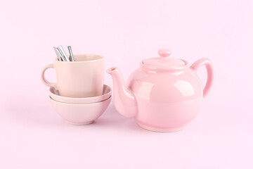 Teapot, bowls and mug with spoons on lilac background