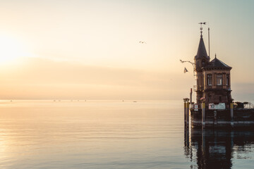 Beautiful sunrise view from Imperia statue to lighthouse at harbor entrance and Lake Constance in...
