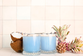 Glasses of cocktail with flowers, baby pineapples and coconut on white tile table