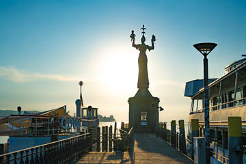 Fototapeta na wymiar Beautiful sunrise view from wooden pier on Imperia statue at harbor entrance and Lake Constance in early morning hours. Steamer harbor, Constance, Baden-Württemberg, Germany, Europe.