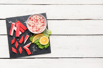 Slate board with tasty crab sticks on light wooden background © Pixel-Shot