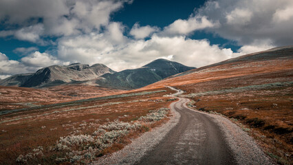 Hiking in Rondane national park with winding path and mountains on a cloudy sky
