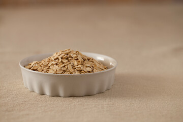 Oat flakes, cereal in a white ceramic bowl on a linen tablecloth on the table, copy space