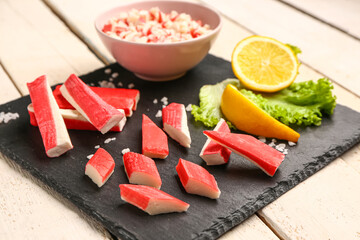 Slate board with tasty crab sticks on light wooden background © Pixel-Shot
