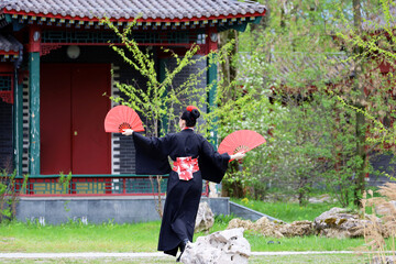 Girl in a traditional asian dress dancing in garden with fans in her hands. Asian beauty and culture
