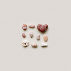 Top view close up small pebbles, sea stone shape heart on sand color background. Square composition from natural stones natural tones. Minimal style. Creative summer pattern, love concept.