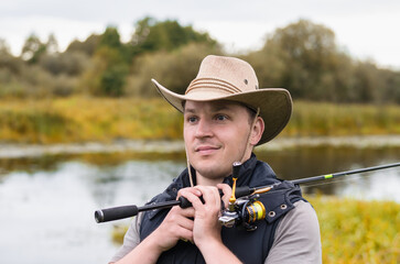 Obraz premium Fisherman in a hat and glasses on the river bank with a spinning rod in his hands.