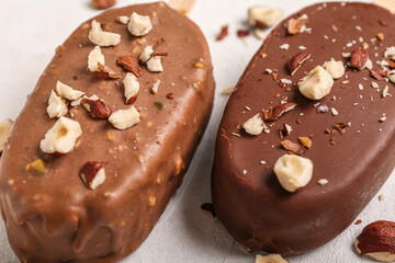 Delicious chocolate covered ice cream with crushed nuts on white table, closeup