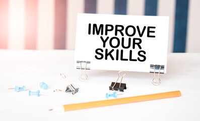 IMPROVE YOUR SKILLS sign on paper on white desk with office tools. Blue and white background