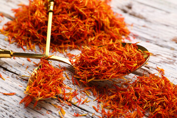 Spoons with pile of saffron on white wooden background