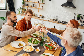 cheerful gay man clinking wine glasses with boyfriend and parents near family supper in modern kitchen. 