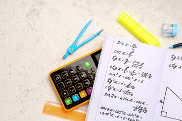 Copybook with maths formulas, calculator and stationery on white grunge background