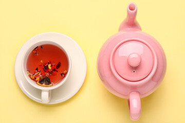 Ceramic teapot with cup of fruit tea on yellow background