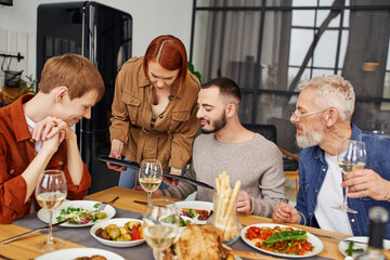 young gay partners looking at photo album during delicious family supper in kitchen. 
