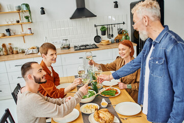young redhead man clinking wine glasses with boyfriend and parents near supper served in modern...