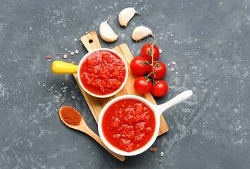 Bowls with tasty tomato sauce and fresh vegetables on blue background