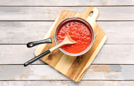 Saucepan with tasty tomato sauce on light wooden background