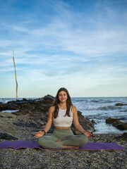Fototapeta na wymiar Caucasian girl is doing yoga on the beach near the sea. In the background the mediterranean sea at sunset.