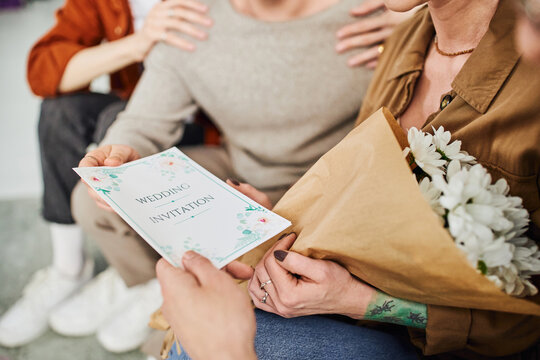 selective focus of wedding invitation near young gay couple and parents sitting at home. 