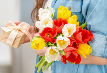 woman with a bouquet of tulips and a gift box in her hands close-up
