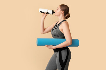 Sporty young woman with yoga mat and bottle of water on beige background