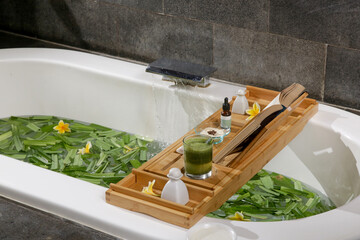 Tub full of water and herbs with wooden bathtub tray with various cosmetic products, relaxation and wellbeing concept of lifestyle  © triocean