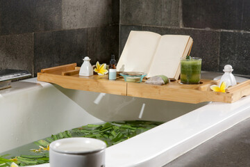 Tub full of water and herbs with wooden bathtub tray with various cosmetic products, relaxation and...