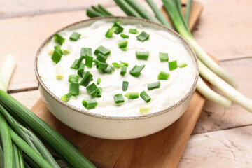 Bowl of tasty sour cream with green onion on light wooden background