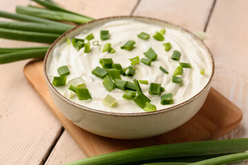 Bowl of tasty sour cream with green onion on light wooden background