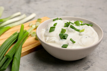 Bowl of tasty sour cream with green onion on grunge background