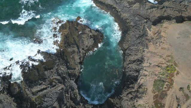 Vue aérienne sur une eau bleu qui s'engouffre dans les rochers sur le littoral