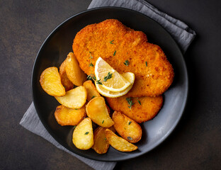 Chicken schnitzel with sauce, fried potatoes and lemon in a plate