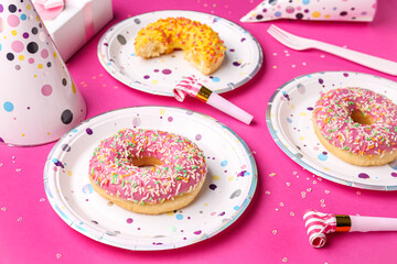 Paper disposable plates with donuts and party blowers on pink background, closeup