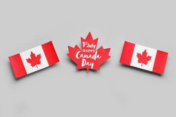 Paper maple leaf with text 1TH JULY HAPPY CANADA DAY and flags on grey background